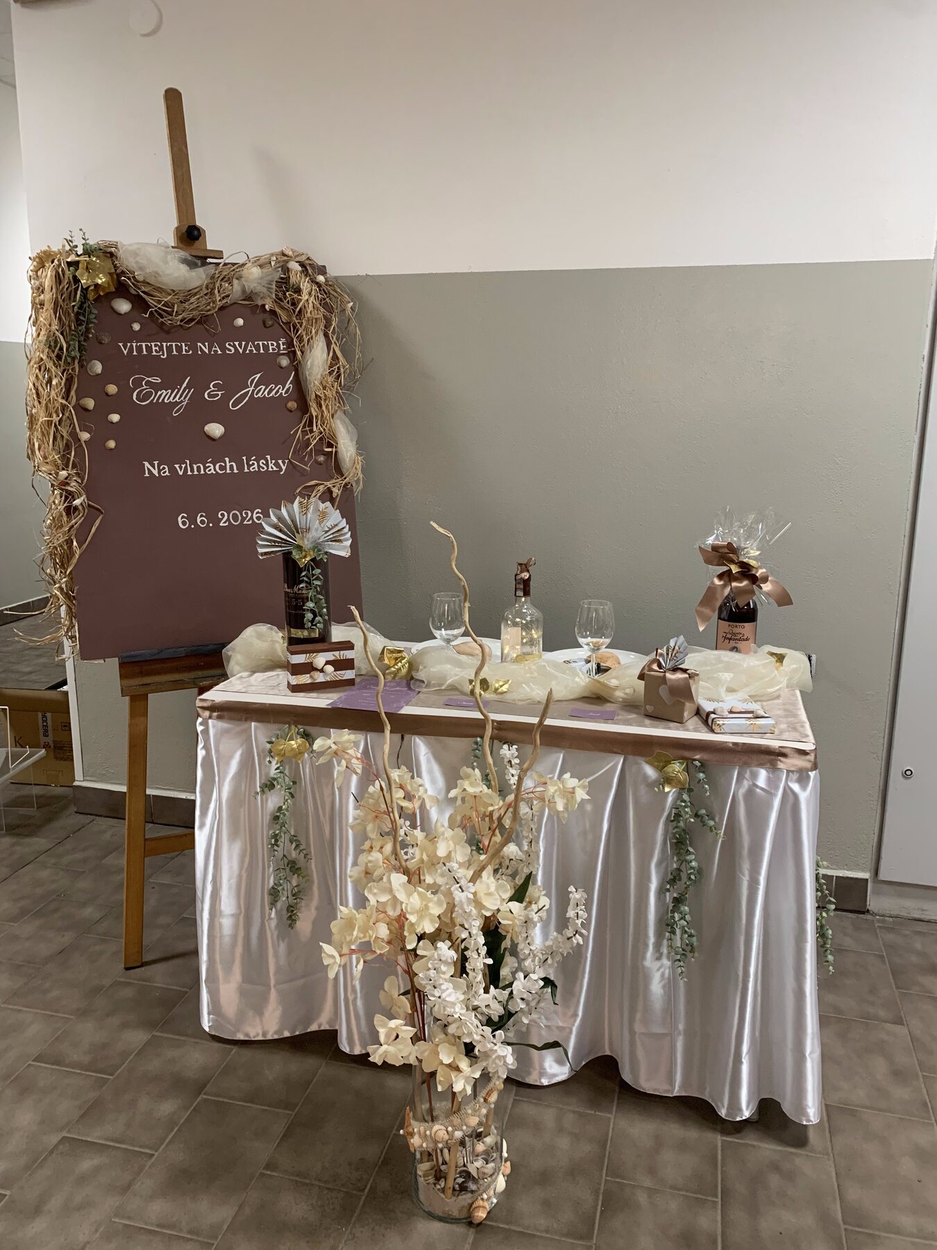 Uvítací tabule se jmény snoubenců Emily a Jacob, květinovou vazbou a dřevěnou cedulí — svatební branding CLAUDIAdesign